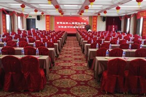Un salón de banquetes con filas de mesas, sillas rojas y un escenario al frente.