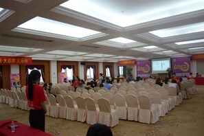 Un salón de conferencias con filas de sillas, un atril y una pantalla para presentaciones.