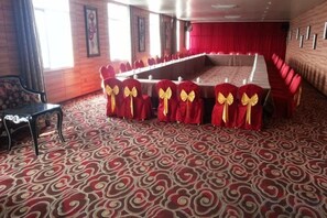 Un salón de banquetes con una larga mesa, sillas rojas con lazos amarillos y alfombra estampada.