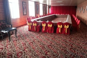 Un salón de banquetes con una larga mesa, sillas rojas con lazos amarillos y alfombra estampada.