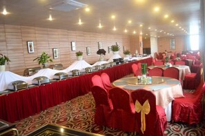 Une salle de banquet avec des tables rondes, des chaises rouges et une longue table de buffet.