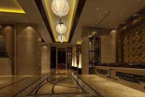 Een hotel lobby met een marmeren vloer, een kroonluchter en een receptiebalie.