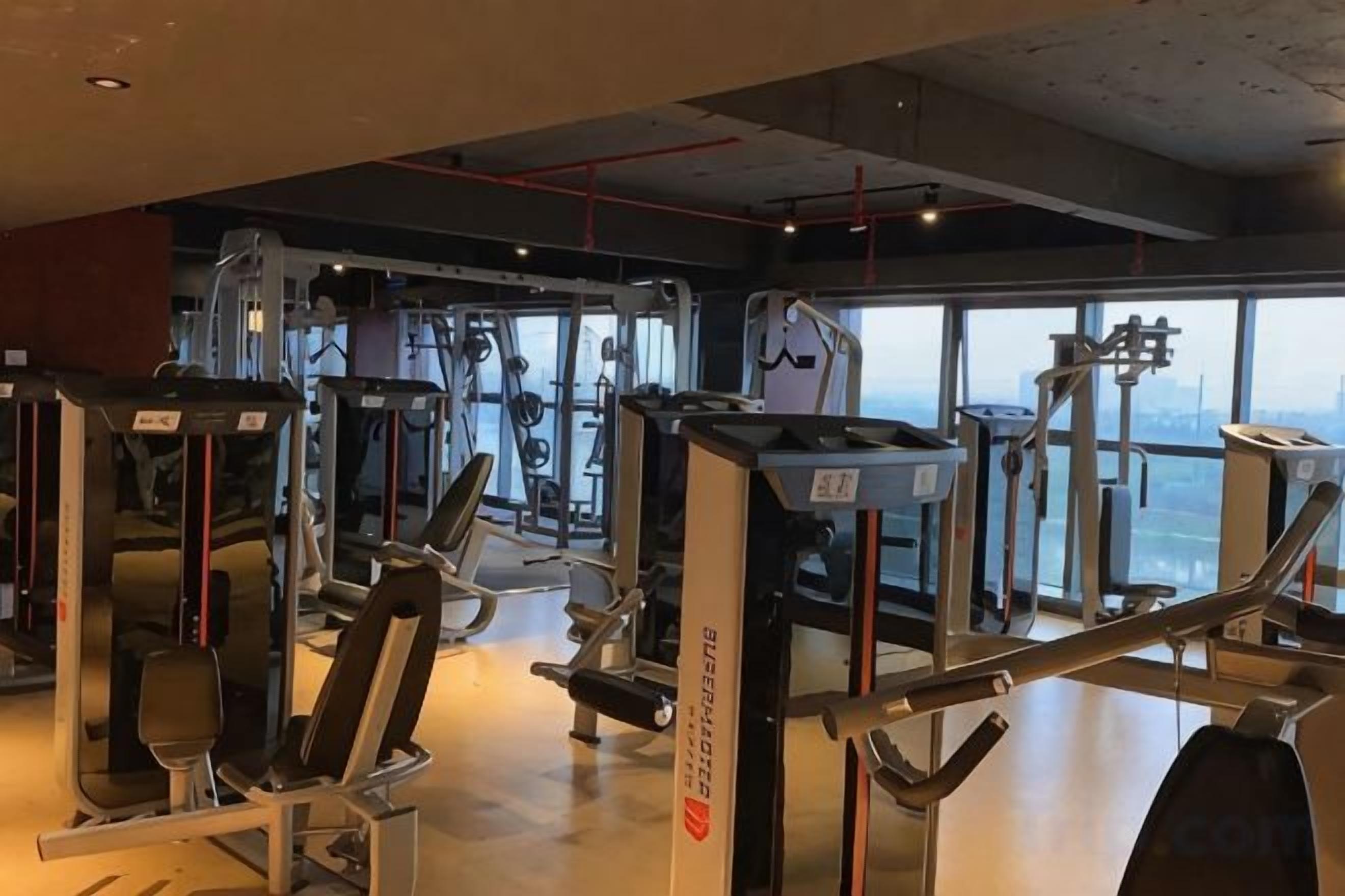 Een fitnessruimte met diverse trainingsapparaten, grote ramen en een hoge nok.