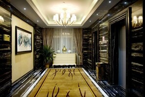 Un vestíbulo de hotel con piso de mármol, una araña y una mesa consola blanca, además de una obra enmarcada en la pared.
