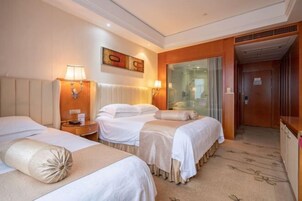 Habitación de hotel con tres camas, un cabecero de madera, un cuadro en la pared y una puerta de vidrio que da al baño.