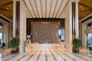 A lobby with a reception desk, marble flooring, and a large wall sculpture. - Vienna International Hotel (Shenzhen)