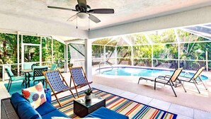 A covered outdoor area with a pool, lounge chairs, and a ceiling fan.