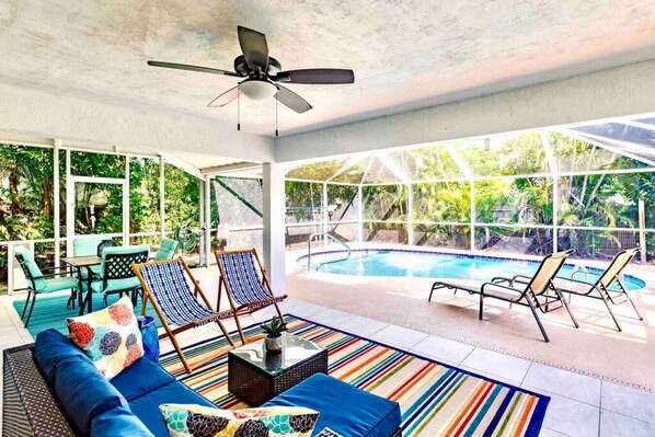 A covered outdoor area with a pool, lounge chairs, and a ceiling fan.