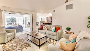 A spacious living room with a sofa set, a coffee table, and a dining area visible through a sliding glass door.