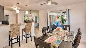 A dining area with a table set for six, surrounded by wicker chairs, a ceiling fan, and pendant lights.