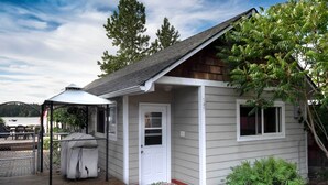 A small cabin with a covered porch, a grill, and a door leading to the main entrance. - Charming Lakefront Cabin w/ Deck & Fire Pit! (Newport)