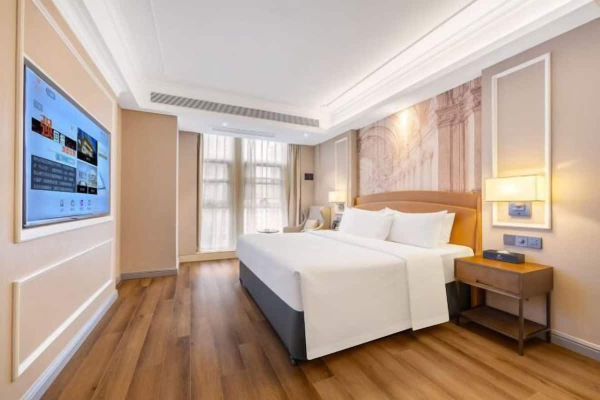 Une chambre d’hôtel avec un grand lit, une table de chevet avec une lampe, un téléviseur fixé au mur et une fenêtre avec des rideaux.