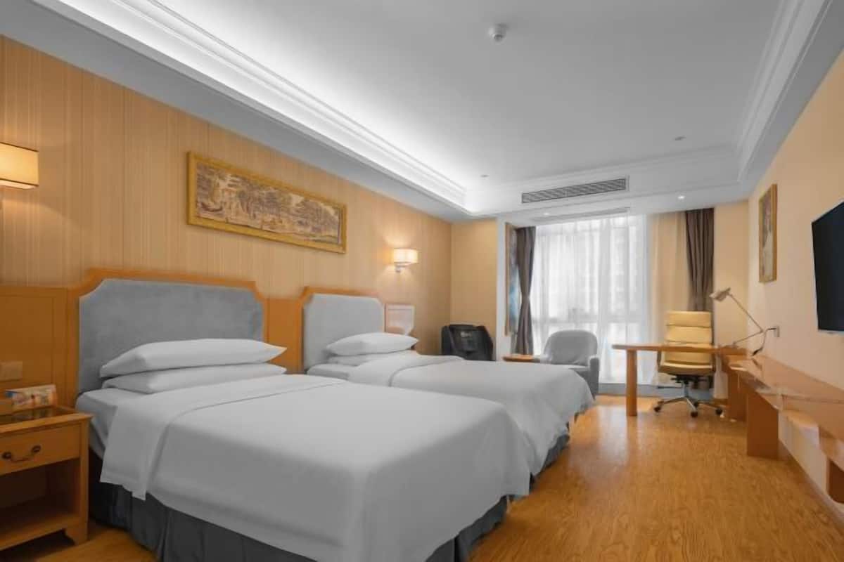 Une chambre d’hôtel avec deux lits, un bureau, une chaise et une télévision.