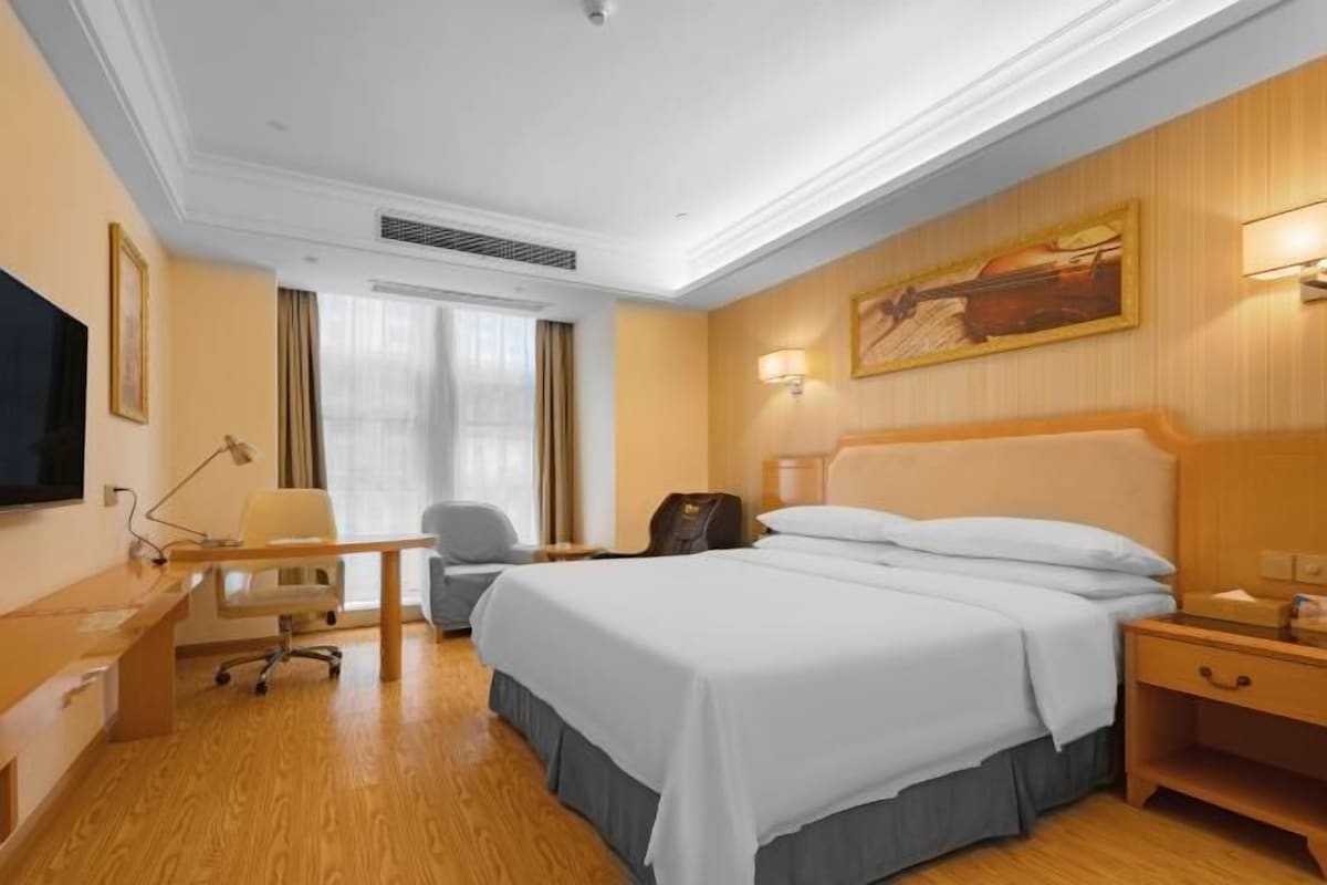 Une chambre d’hôtel avec un grand lit, un bureau, une chaise, une télévision et un tableau au mur.