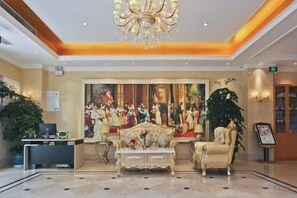 En lobby med reception, et stort maleri, en lysekrone og et siddeområde.