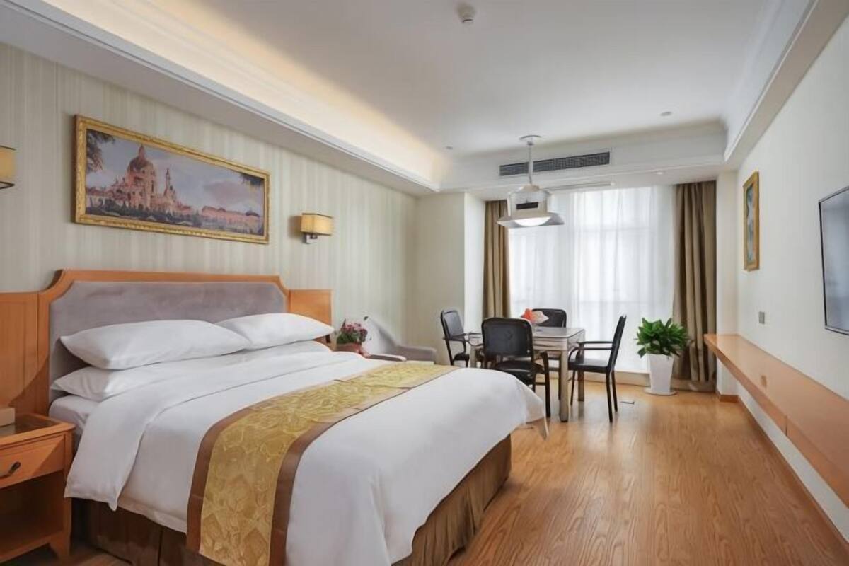 Une chambre d’hôtel avec un lit, un bureau, une chaise et une plante en pot.