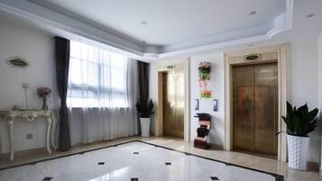 Een hotellobby met een marmeren vloer, twee liften, een receptiebalie en een groot raam met gordijnen.