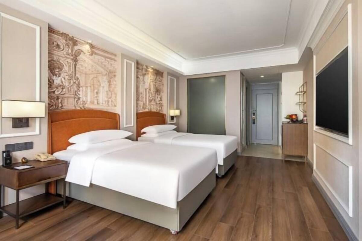 Une chambre d’hôtel avec deux lits, un bureau avec une lampe, une télévision et un mur décoratif.