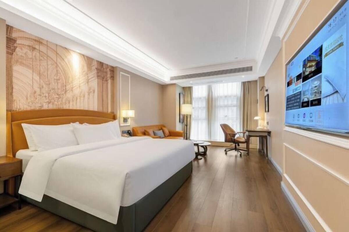 Une chambre d’hôtel avec un grand lit, un bureau, une chaise et un téléviseur fixé au mur.
