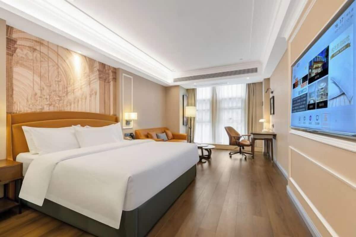A hotel room with a large bed, a desk, a chair, and a wall-mounted TV.