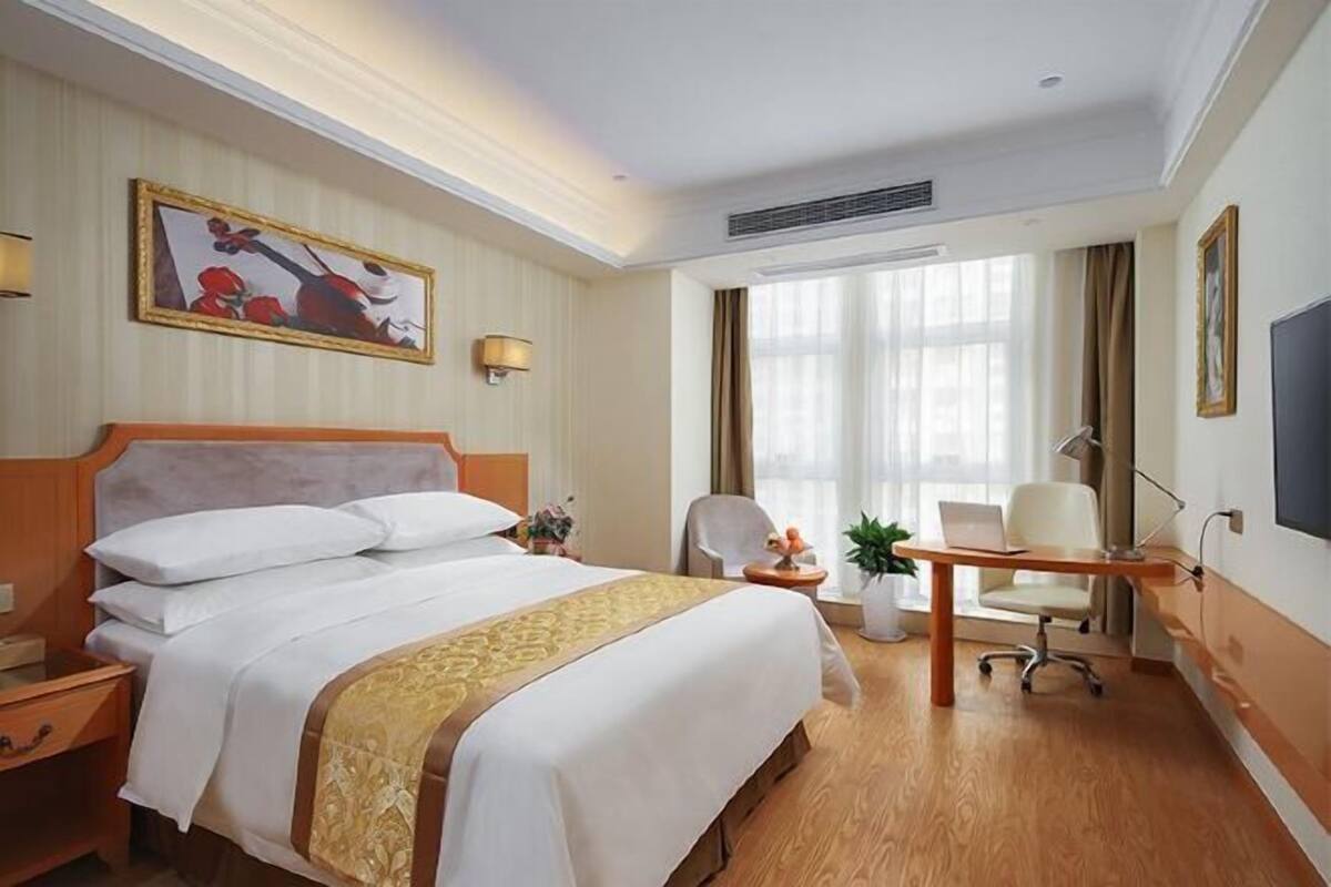 Une chambre d’hôtel avec un lit, un bureau, une chaise et de grandes fenêtres.
