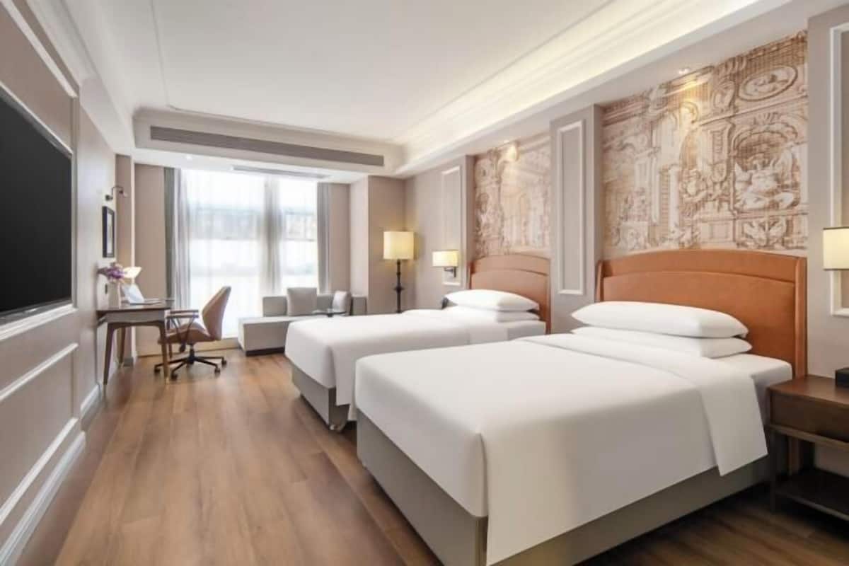 Une chambre d’hôtel avec deux lits, un bureau, une chaise et une grande fenêtre.