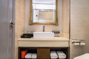 Ein Badezimmer mit einem weißen Waschbecken, einem spiegel mit goldener Rahmung und einem Handtuchhalter.