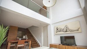 Un saló modern amb escala, zona de menjador i televisió de pantalla plana sobre un moble de fusta.