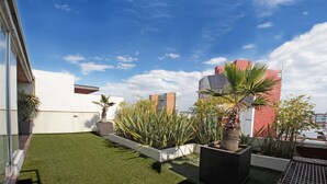 Un jardí al terrat amb gespa artificial, plantes en testos i vistes als edificis circumdants.