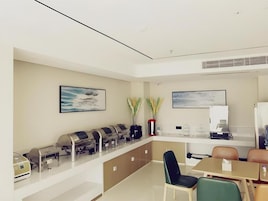 Una habitación de hotel moderna con kitchenette, zona de comedor con mesa y sillas, y obras de arte en las paredes.