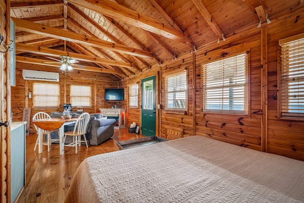 A log cabin interior with a bed, a dining area, a kitchen, and a television.