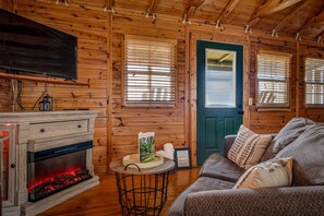 A cozy cabin interior with a fireplace, wooden walls, a couch, and a door.