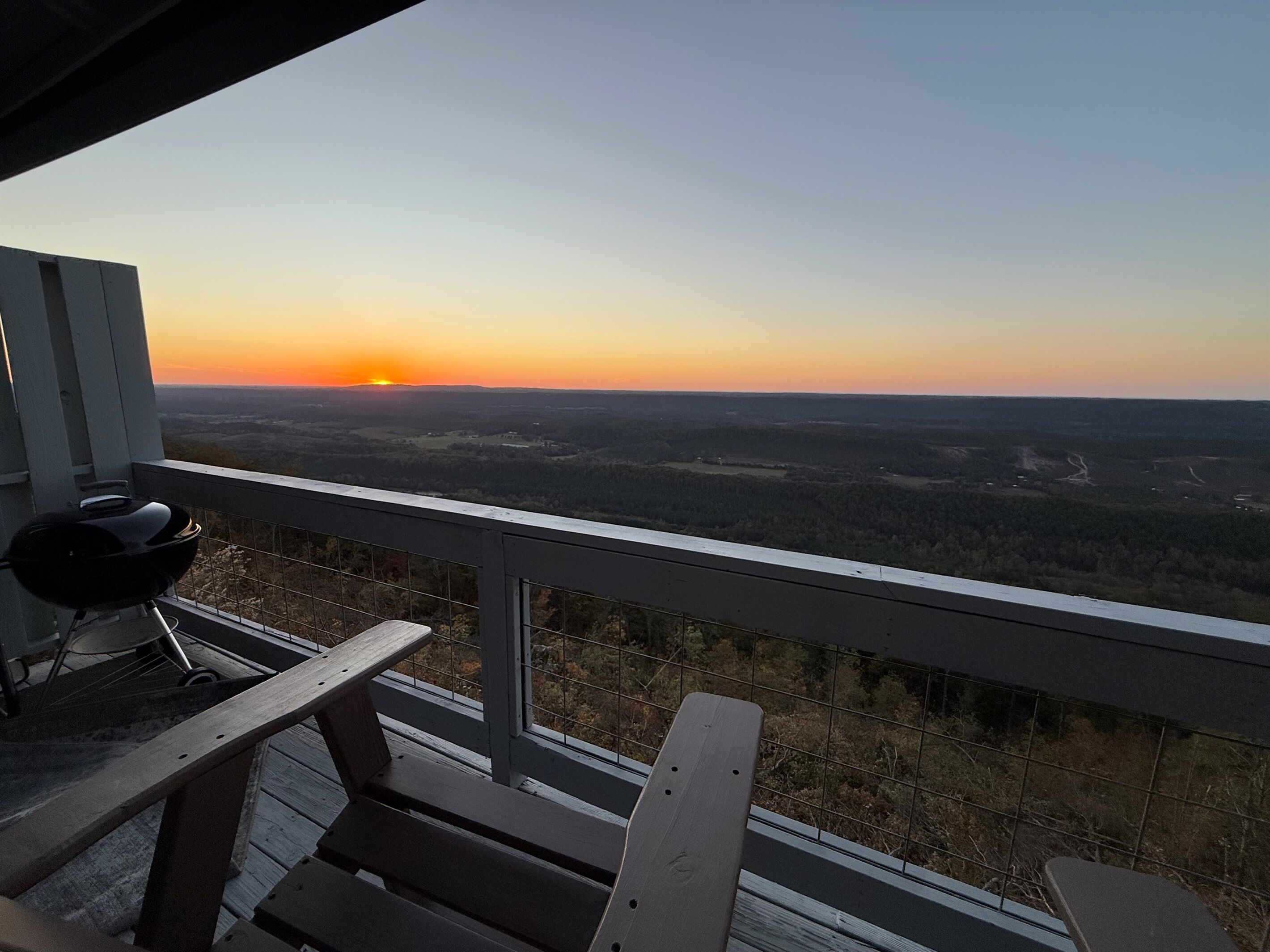 Ein Balkon mit Blick auf einen Sonnenuntergang über einer bewaldeten Landschaft.