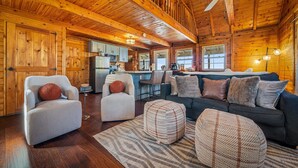 Ein großzügiger Wohnbereich mit hoher Decke, Holzwänden und einer gemütlichen Sitzecke mit Sofa, Sesseln und Hocker.