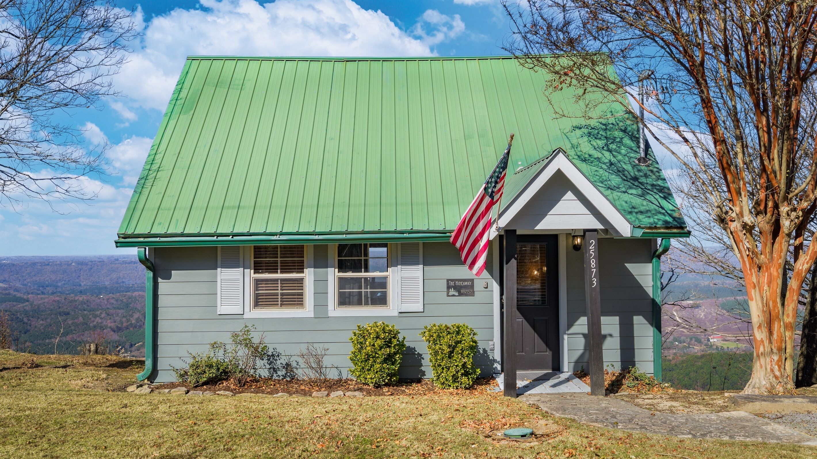 A small house with a green roof, an American flag, and a sign that reads "The Hideaway."