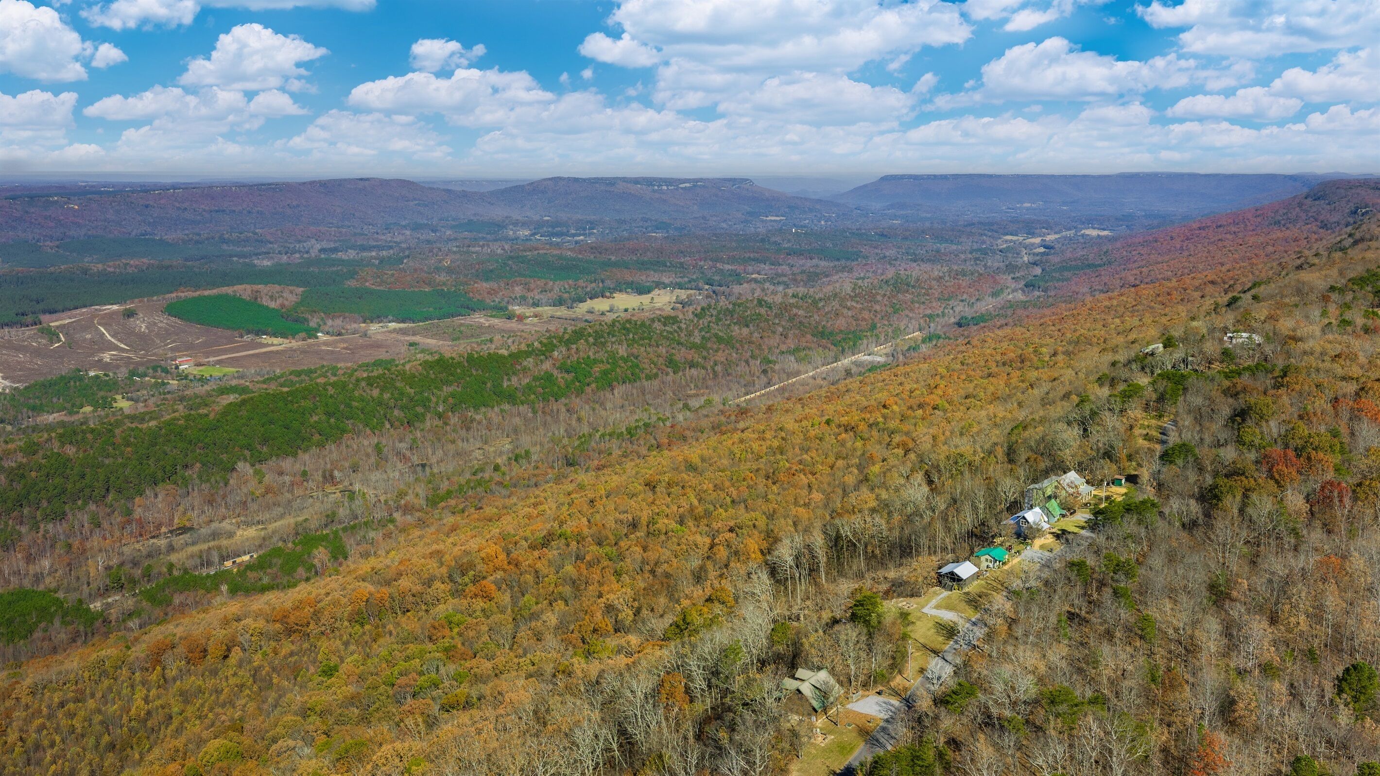 A mountainous landscape with autumn foliage, a winding road, and scattered buildings.