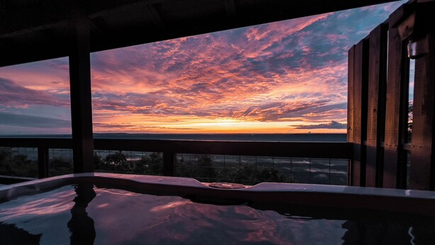 Ein Pool, der einen Sonnenuntergang reflektiert, mit Blick auf den Himmel und die ferne Landschaft.