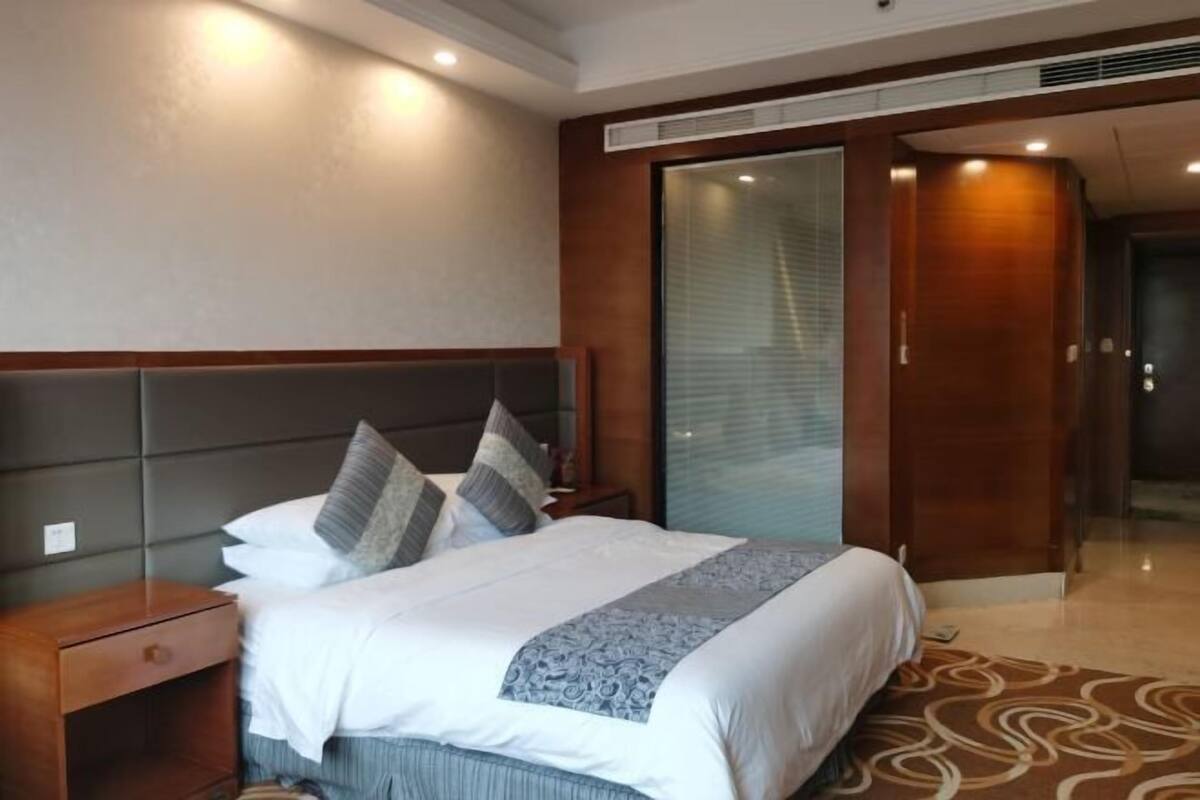 A hotel room with a large bed, a wooden headboard, a nightstand, and a sliding door leading to a bathroom.