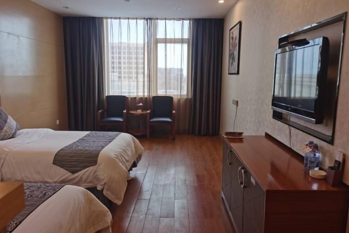 A hotel room with two beds, a desk, a TV, and a window with curtains.
