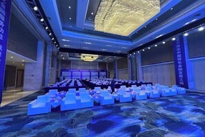 A large conference room with rows of white chairs and tables, a stage with a large screen, and a blue carpet with a leaf pattern. - Ruixiang International Hotel (Quanjiao)