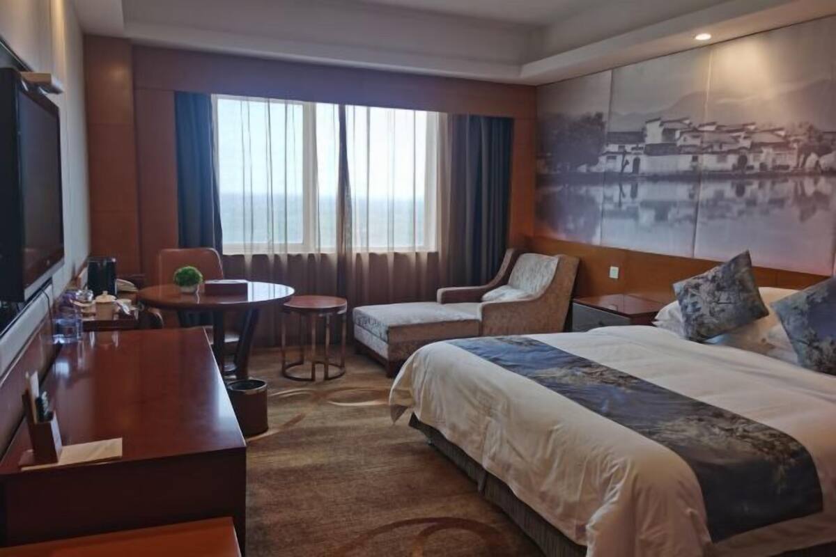A hotel room with a large bed, a desk, a chair, a small table, and a TV.