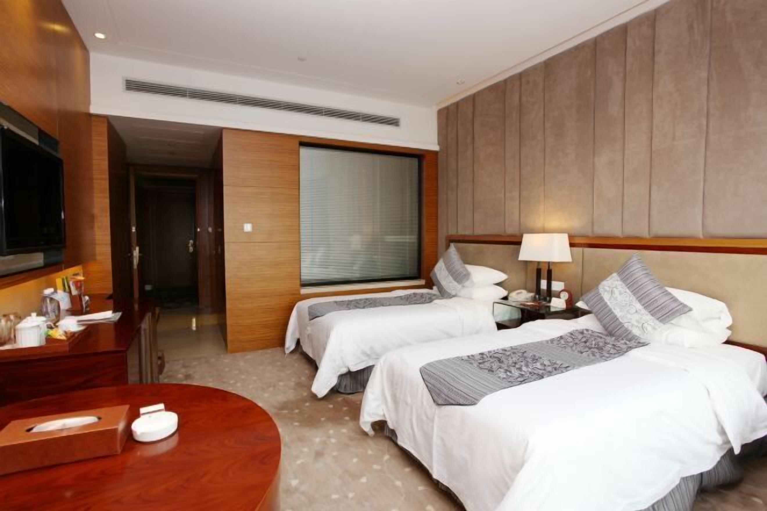 A hotel room with two beds, a TV, a desk with a lamp, and a bedside table.