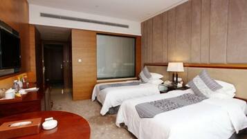 A hotel room with two beds, a TV, a desk with a lamp, and a bedside table.