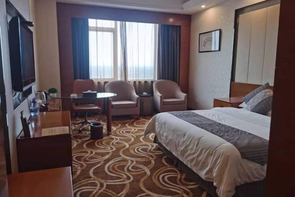 A hotel room with a bed, a desk with a chair, a small table, and a TV.