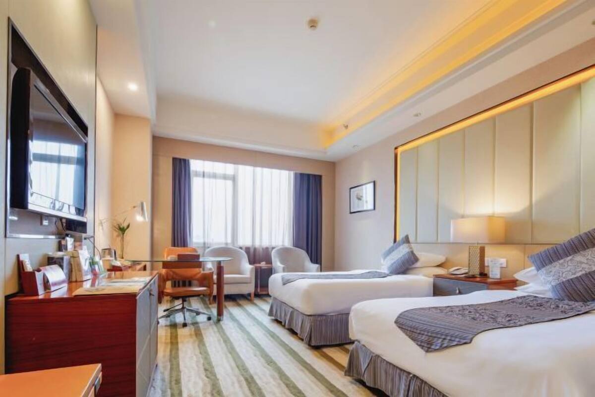 A hotel room with two beds, a desk, a chair, a TV, and a large mirror.