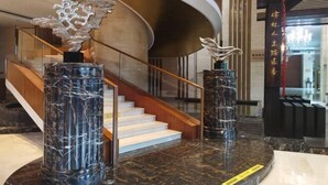 A modern lobby with a curved staircase, marble columns, and a decorative metal sculpture. - Ruixiang International Hotel (Quanjiao)