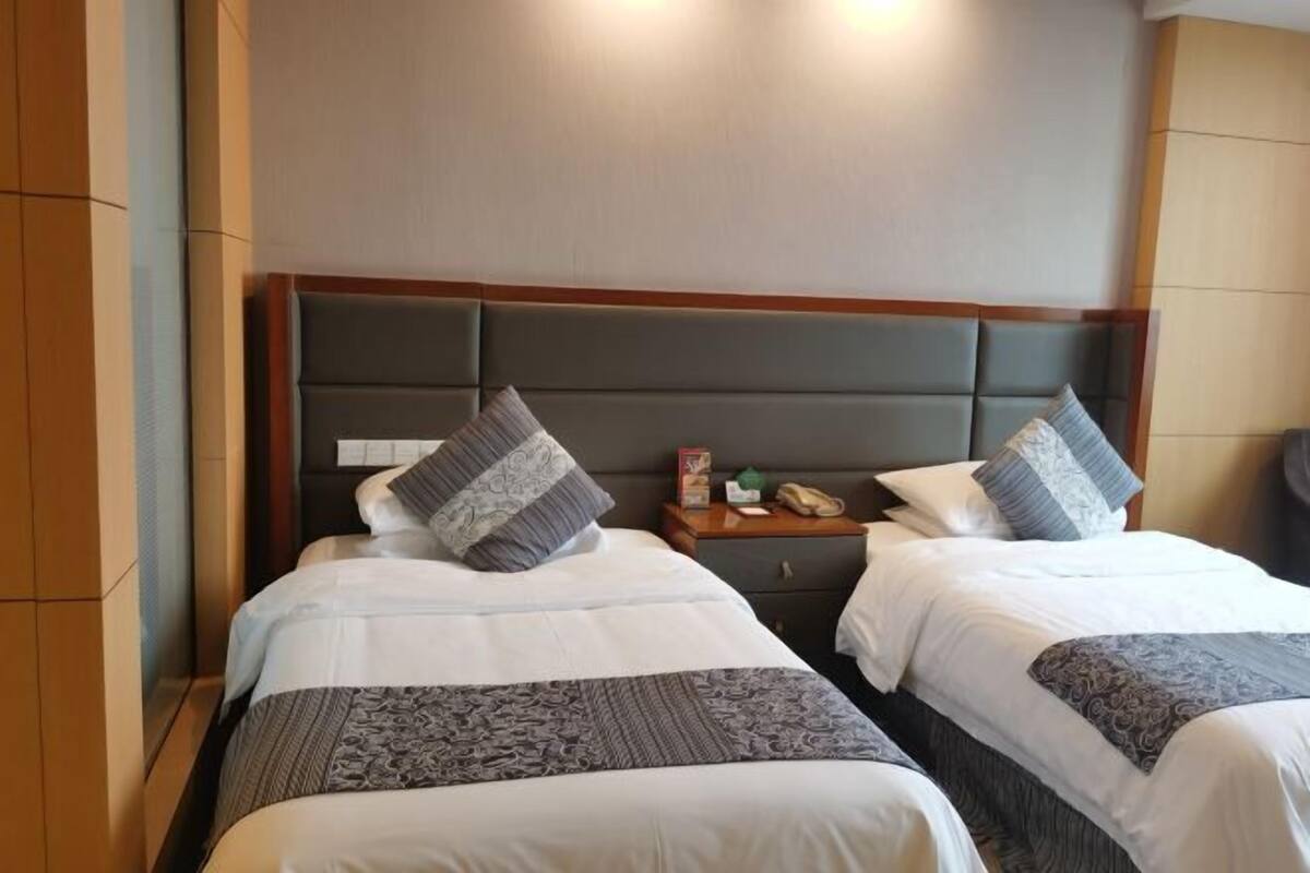 A hotel room with two beds, a wooden headboard, a nightstand with a phone, and a small table with a lamp.