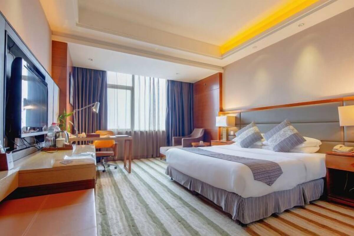 A hotel room with a large bed, a desk, a TV, and a window with curtains.