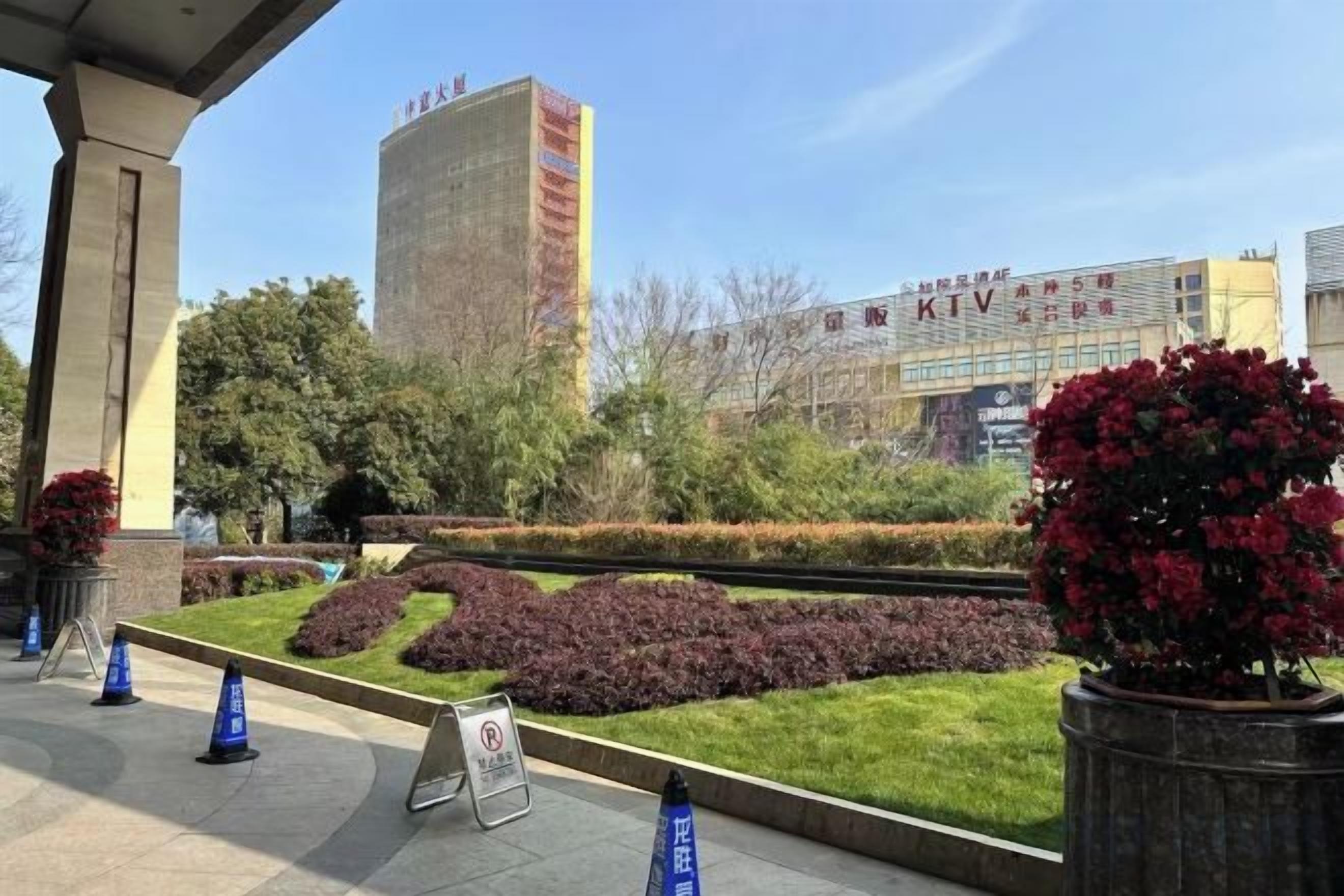 A landscaped area with a building in the background, a sign, and a few potted plants.