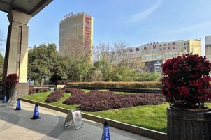 Zona ajardinada con un edificio al fondo, un letrero y algunas plantas en macetas.